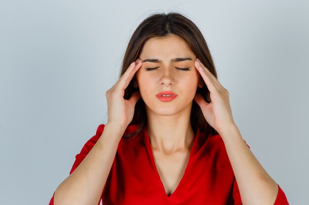 Young lady rubbing temples in red blouse and looking exhausted