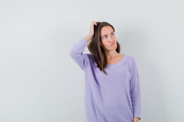 Young lady scratching head in casual shirt and looking pensive 