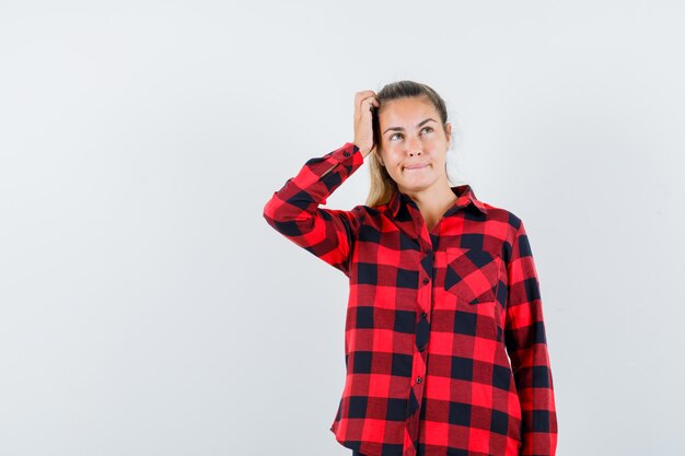 Young lady scratching head in checked shirt and looking hesitant