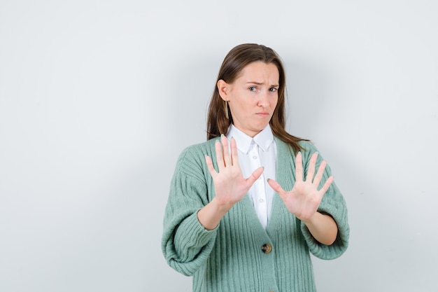 Young lady in shirt, cardigan showing stop gesture and looking sensible , front view.