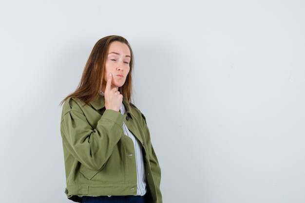 Young lady in shirt holding finger on cheek and looking pensive , front view.