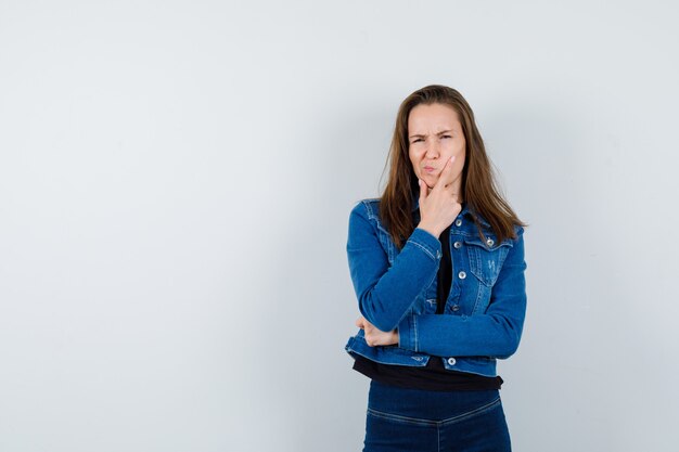 Young lady in shirt, jacket holding her chin and looking pensive , front view.