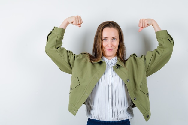 Free photo young lady in shirt, jacket showing muscles of arms and looking confident , front view.