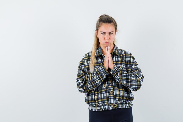 Young lady in shirt, shorts showing namaste gesture and looking pensive , front view.