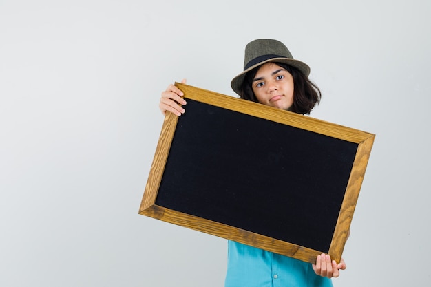 Free photo young lady showing black frame in blue shirt, hat and looking self-confident.