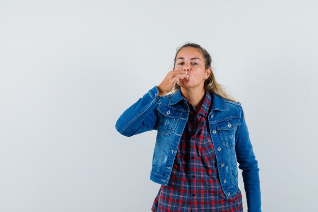 Young lady showing delicious gesture in shirt, jacket and looking delighted. front view.