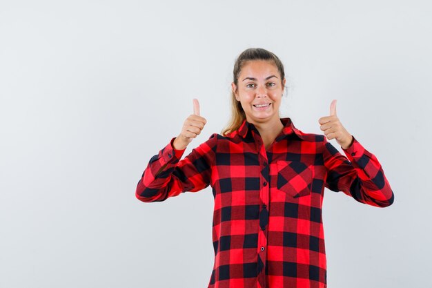 Young lady showing double thumbs up in checked shirt and looking confident