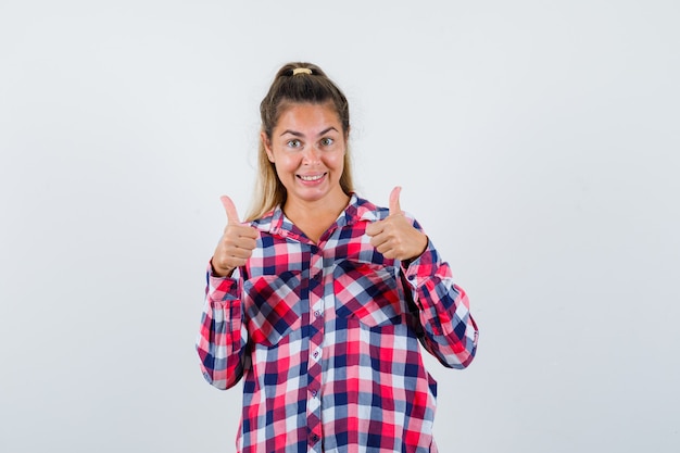 Free photo young lady showing double thumbs up in checked shirt and looking merry. front view.