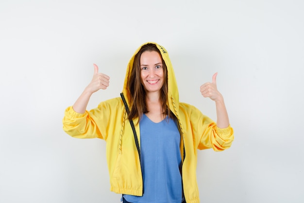 Young lady showing double thumbs up in t-shirt, jacket and looking happy. front view.