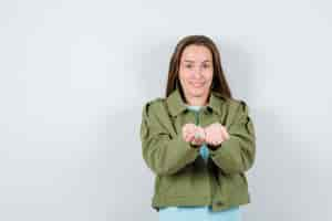 Free photo young lady showing giving or receiving gesture in green jacket and looking cheery , front view.