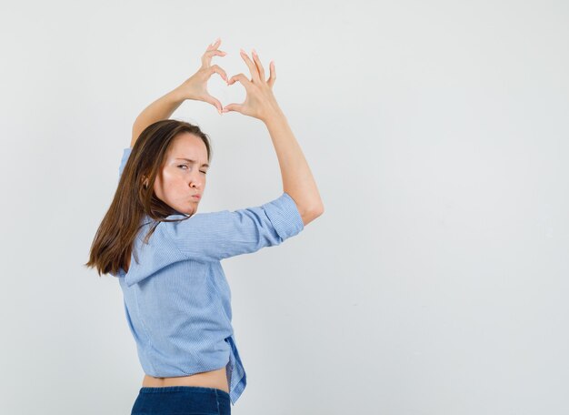 Free photo young lady showing heart gesture, pouting lips, winking eye in blue shirt