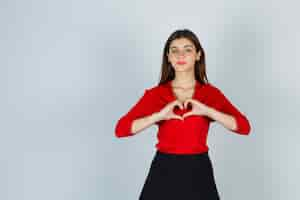 Free photo young lady showing heart gesture in red blouse, skirt and looking gorgeous