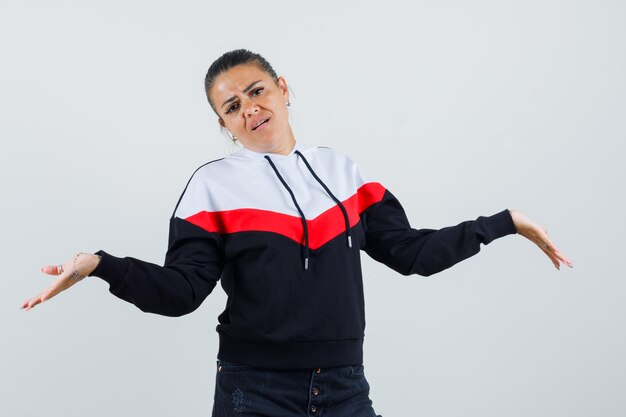 Young lady showing helpless gesture in colorful sweatshirt and looking unhappy , front view.