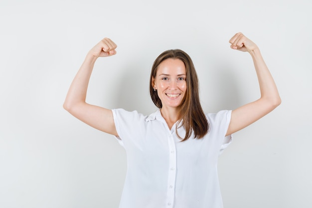 Young lady showing her arm muscles in white blouse and looking healthy