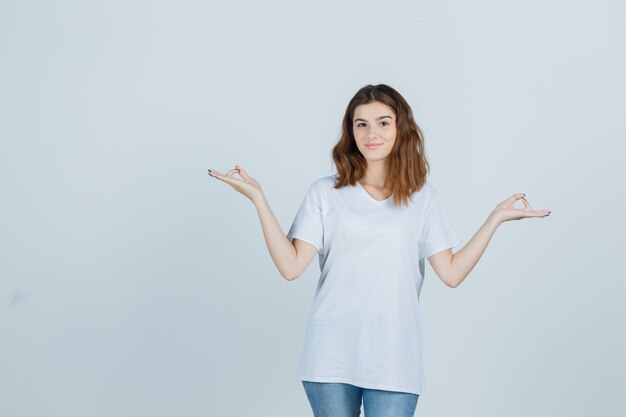 Young lady showing meditation gesture in t-shirt, jeans and looking peaceful , front view.