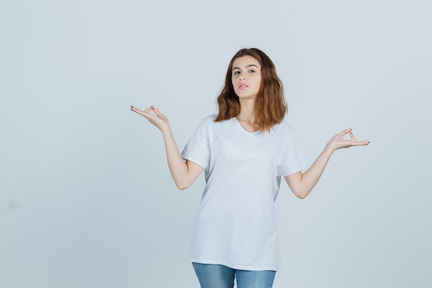 Young lady showing meditation gesture in t-shirt, jeans and looking peaceful , front view.