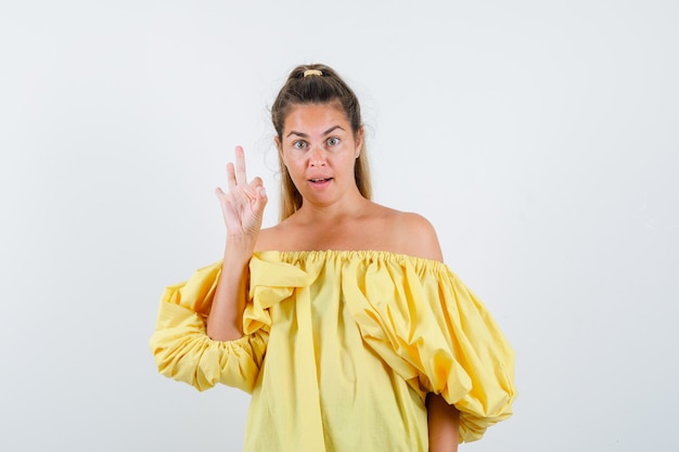 Young lady showing ok gesture in yellow dress and looking confident , front view.