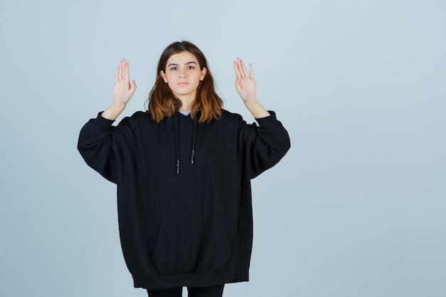 Free photo young lady showing palms in oversized hoodie, pants and looking confident , front view.