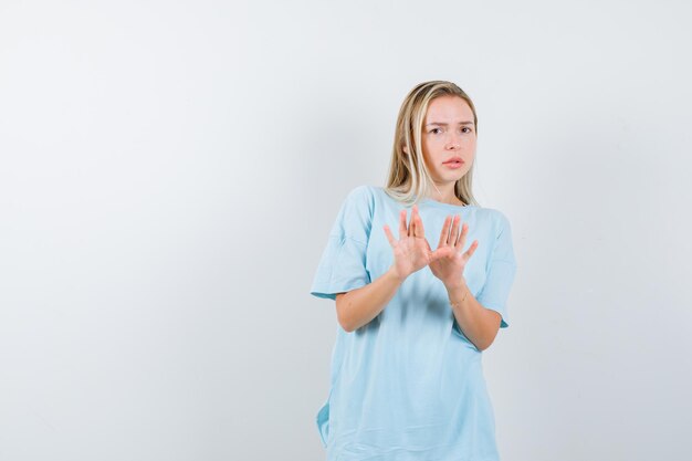 Young lady showing palms in surrender gesture in t-shirt and looking helpless isolated