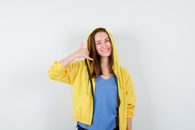 Young lady showing phone gesture in t-shirt, jacket and looking confident. front view.