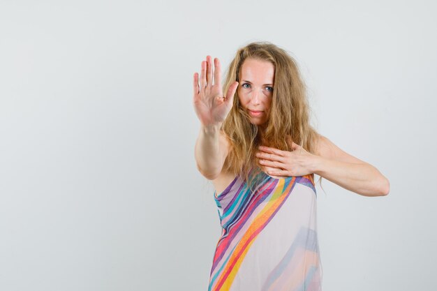 Young lady showing refusal gesture with hand on chest in summer dress and looking confident 