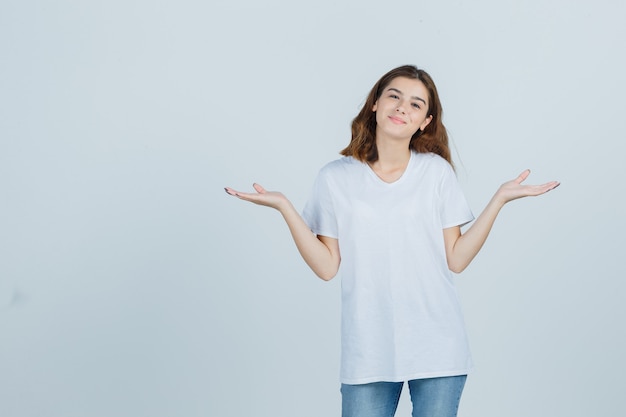 Young lady showing scales gesture in t-shirt, jeans and looking confident. front view.