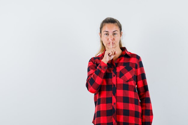 Young lady showing silence gesture in checked shirt and looking confident