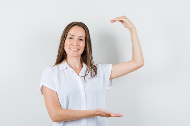 Young lady showing size sign in white blouse front view.