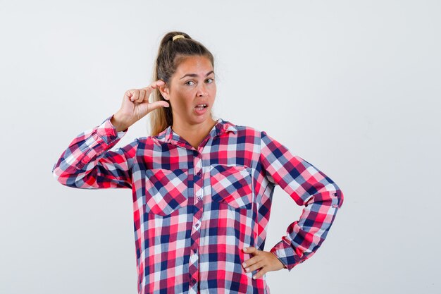 Young lady showing small size sign in checked shirt and looking confident , front view.