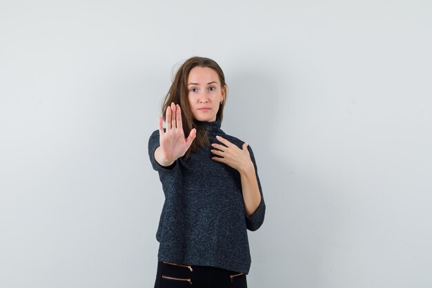 Young lady showing stop gesture in casual shirt and looking confident. front view.