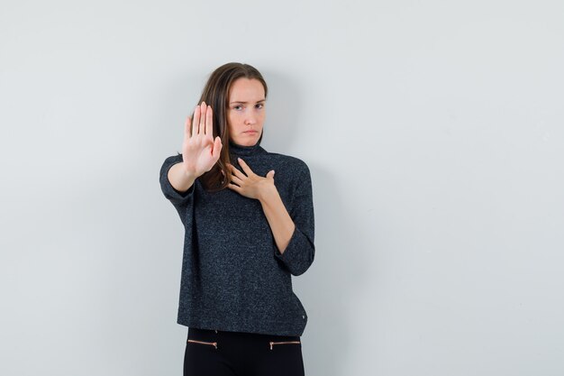 Young lady showing stop gesture in casual shirt and looking resolute. front view.