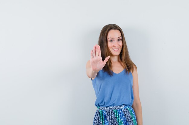 Young lady showing stop gesture in singlet, skirt and looking glad