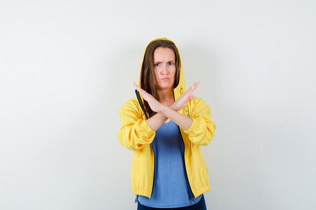 Young lady showing stop gesture in t-shirt, jacket and looking serious. front view.