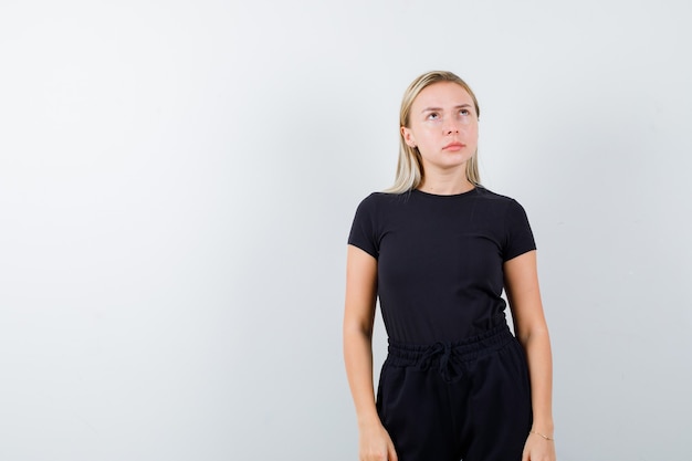 Free photo young lady showing thinking pose in t-shirt, pants and looking gloomy. front view.