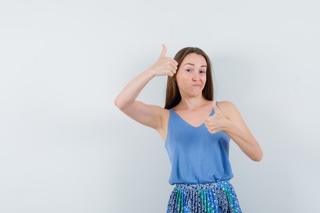 Young lady showing thumb up in blouse,skirt and looking satisfied , front view.