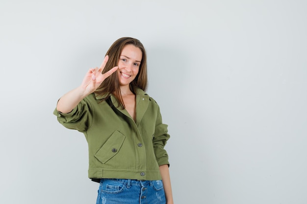 Free Photo young lady showing v-sign in green jacket shorts and looking confident  