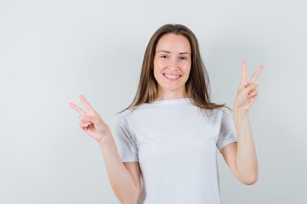 Young lady showing v-sign in white t-shirt and looking happy 