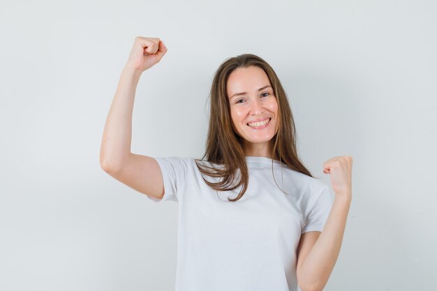 Young lady showing winner gesture in white t-shirt and looking happy