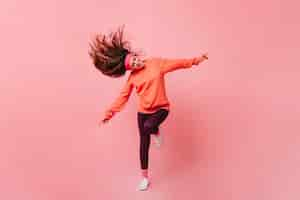 Free photo young lady in sports outfit dancing on pink background full length portrait of woman in orange sweatshirt