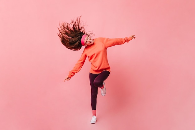 Young lady in sports outfit dancing on pink background Full length portrait of woman in orange sweatshirt