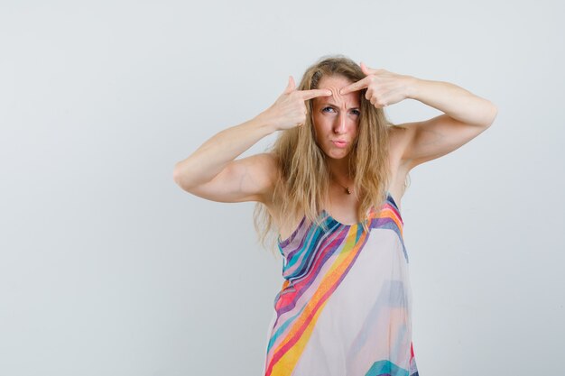 Young lady squeezing her pimple on forehead in summer dress 