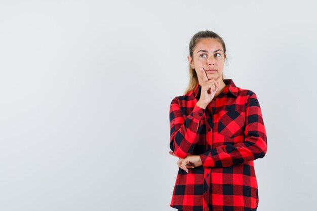 Young lady standing in thinking pose in checked shirt and looking sensible