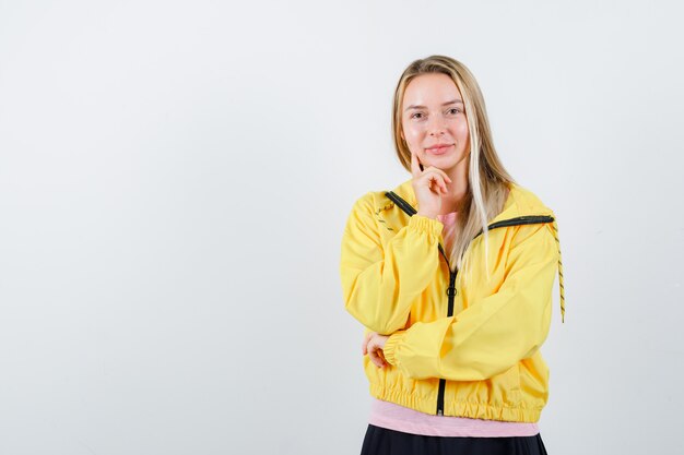 Young lady standing in thinking pose in t-shirt, jacket and looking cheerful