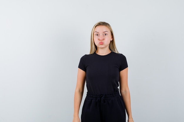 Free photo young lady standing with blown cheeks in t-shirt, pants and looking merry. front view.