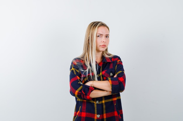 Free photo young lady standing with crossed arms in checked shirt and looking confident. front view.