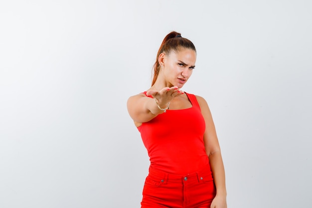 Free Photo young lady stretching out hands towards at camera in red singlet, red trousers and looking careful , front view.