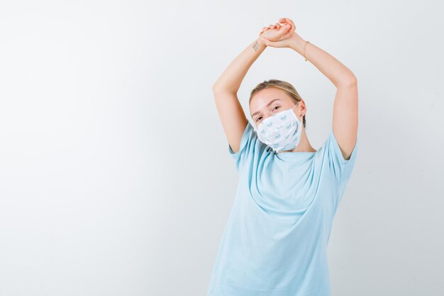 Young lady stretching upper body in t-shirt, mask and looking relaxed