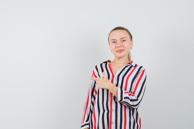 Young lady in striped shirt pointing to the side and looking satisfied