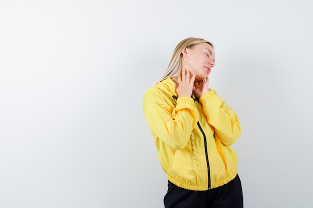 Young lady suffering from neck in yellow jacket, pants and looking tired , front view.