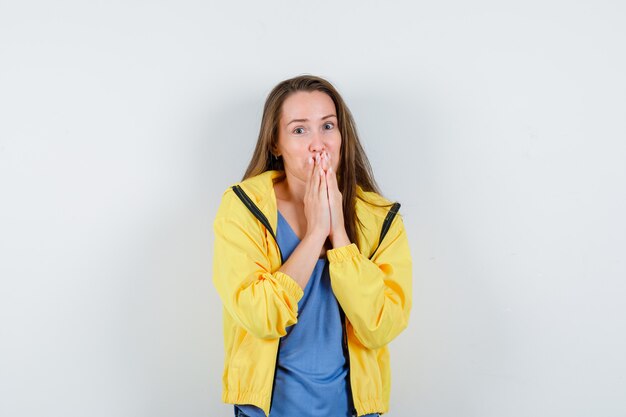 Young lady in t-shirt holding hands on mouth and looking positive , front view.